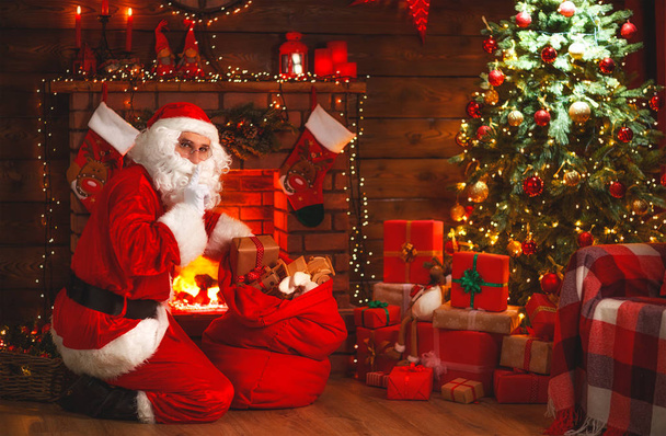 Frohe Weihnachten! Weihnachtsmann neben Kamin und Baum mit Geschenk - Foto, Bild