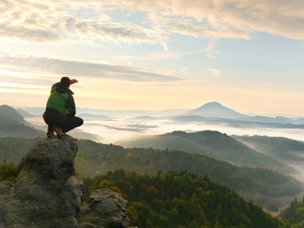 El hombre permanece en el pico rocoso durante el amanecer y vigila el paisaje brumoso
. - Foto, Imagen
