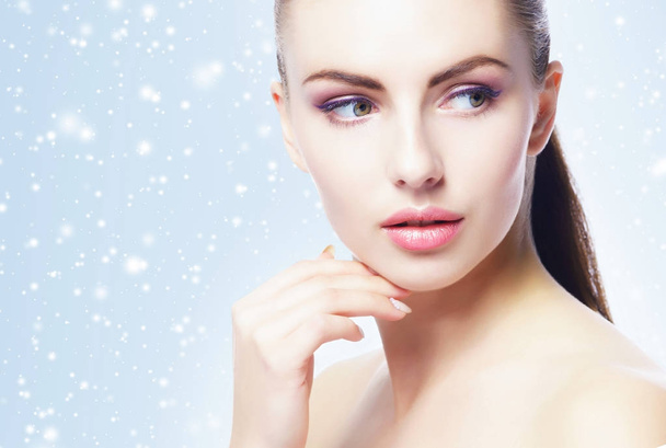 closeup portrait of young, beautiful, fresh and healthy woman over blue background with snowflakes - Foto, immagini