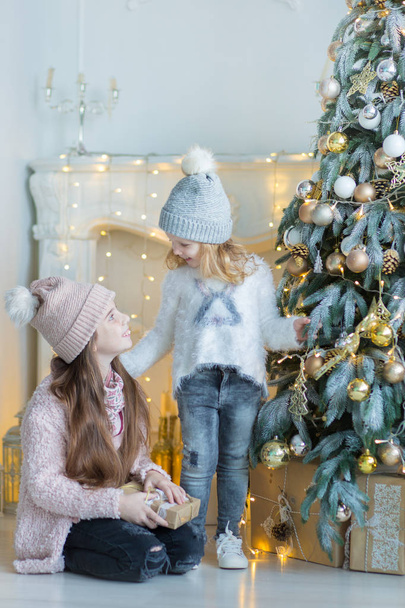 Two cute awesome girls sisters celebrating New Year Christmas close to xmas tree full of toys in stylish dresses with candies - Foto, Imagem