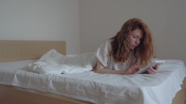 Good looking red-hairs girl with a digital tablet in her bedroom - Materiał filmowy, wideo