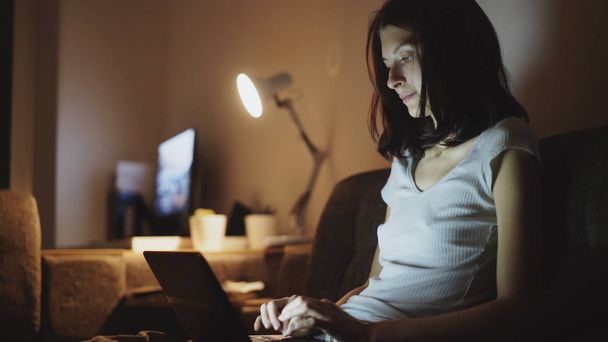 Young attractive woman sharing social media using on laptop computer at home in night time - Foto, Imagen