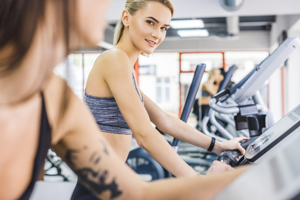 close-up shot of sportive women working out on elliptical machines at gym - Photo, Image