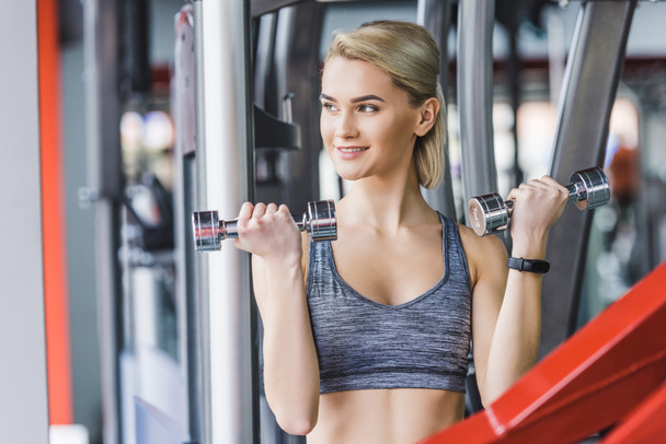 smiling young woman working out with dumbbells at gym - Фото, зображення