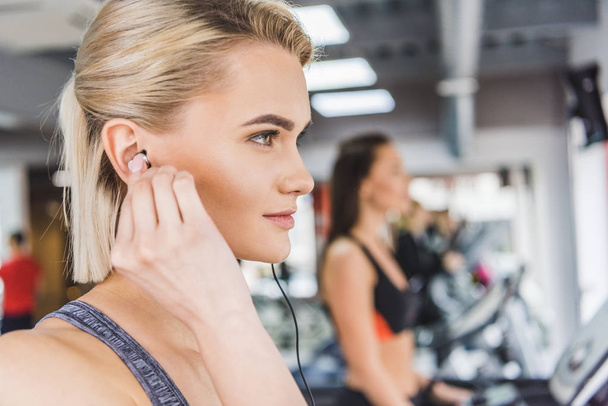 close-up portrait of young beautiful woman listening music with earphones at gym - Photo, Image