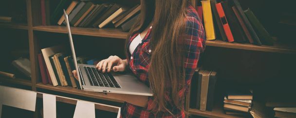 Young woman holds a laptop and book shelves on background - Foto, afbeelding