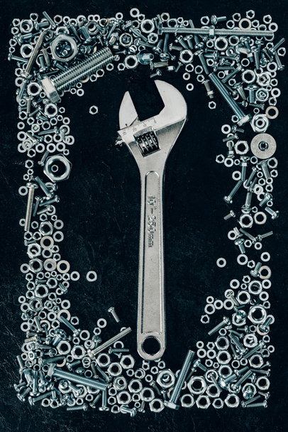 верхний вид металлического гаечного ключа, винтов и клинчеров на темном столе
 - Фото, изображение