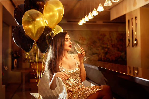 Glamour beautiful  smiling woman with champagne and golden ballons on background in a restaurant selebrating new year, christmas, x-mas - 写真・画像