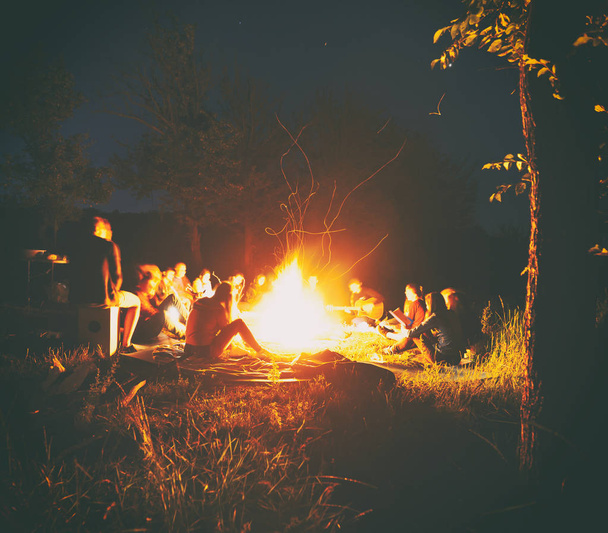The company of young people are sitting around the bonfire and s - Foto, Bild