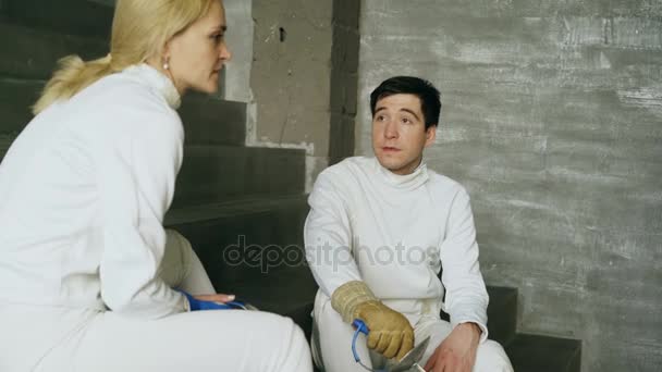 Two fencers man and woman sharing experience during break of fencing match indoors - Séquence, vidéo