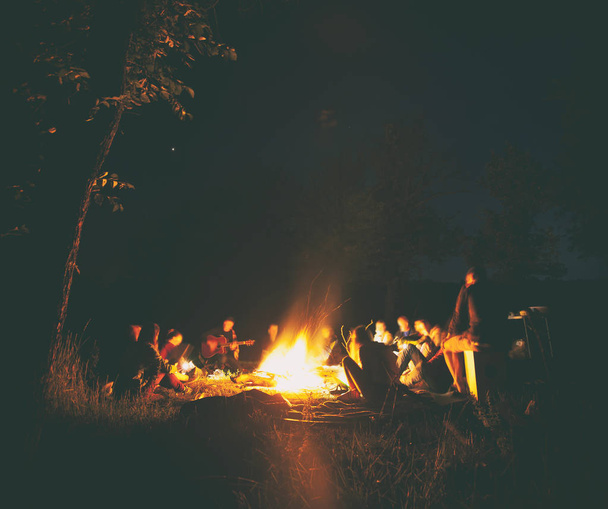 The company of young people are sitting around the bonfire and s - Valokuva, kuva