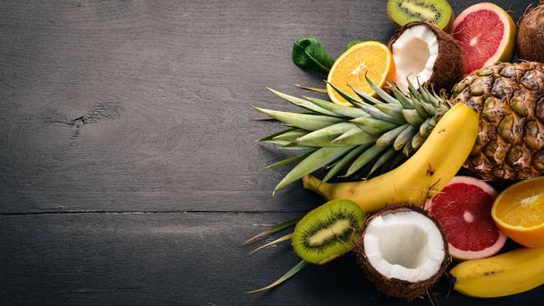 Fresh Tropical Fruits. Pineapple, coconut, kiwi, orange, pomegranate, grapefruit. On a wooden background. Top view. Free space for text. - Foto, afbeelding