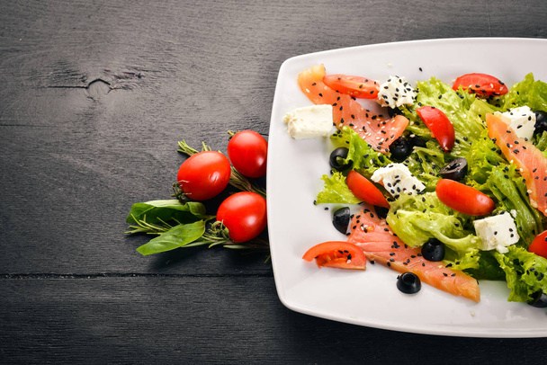 Salmon salad, feta cheese, salad leaves and fresh vegetables on the plate. On a wooden background. Top view. Free space for text. - Фото, зображення