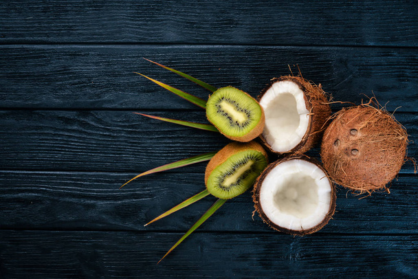 Coconuts and kiwi on a wooden background. Tropical fruits and nuts. Top view. Free space for text. - Фото, изображение