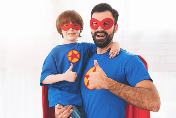 Pai e filho de fato vermelho e azul de super-heróis. Em seus rostos há máscaras e eles estão em capas impermeáveis
. - Foto, Imagem