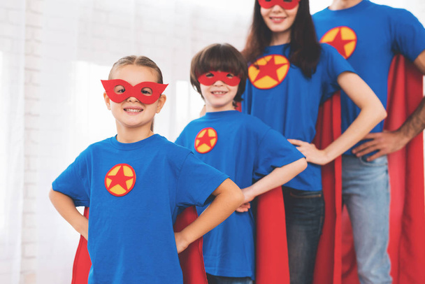 junge Familie in roten und blauen Anzügen von Superhelden. ihre Gesichter in Masken und sie sind in Regenmänteln. - Foto, Bild