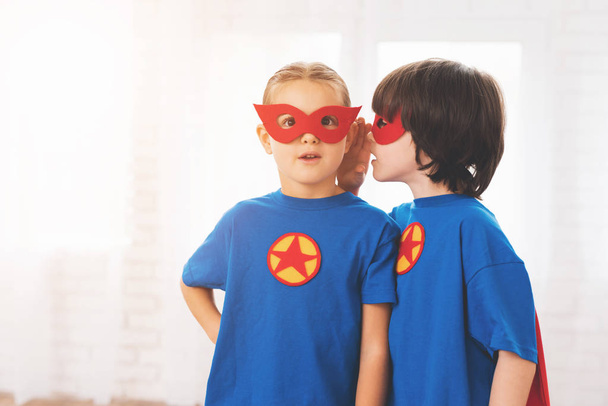 Bambini con le tute rosse e blu dei supereroi. Indossano delle maschere. Bambini in posa in camera luminosa
. - Foto, immagini