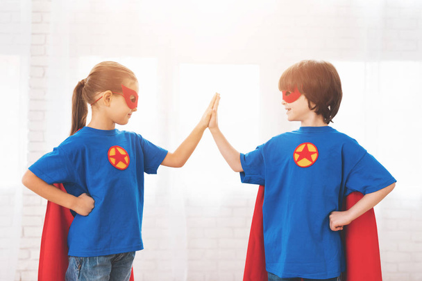 Enfants dans les costumes rouges et bleus de super-héros. Ils portent des masques. Enfants posant dans une chambre lumineuse
. - Photo, image