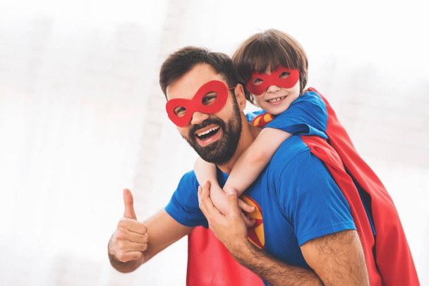 Father and son in the red and blue suits of superheroes. On their faces are masks and they are in raincoats. - Fotoğraf, Görsel