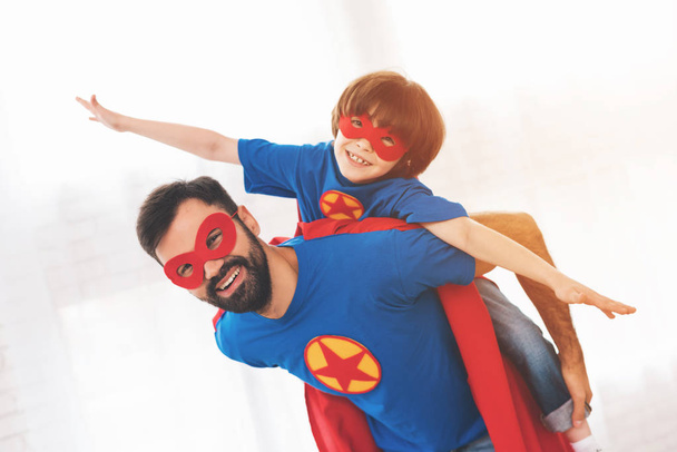 Ojciec i syn w kolorach czerwonym i niebieskim superbohaterów. Na ich twarze są maski i są one w płaszcze. - Zdjęcie, obraz
