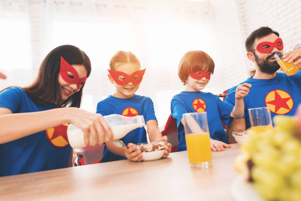 Família jovem em ternos vermelhos e azuis de super-heróis. Seus rostos em máscaras e eles estão em capas impermeáveis
. - Foto, Imagem
