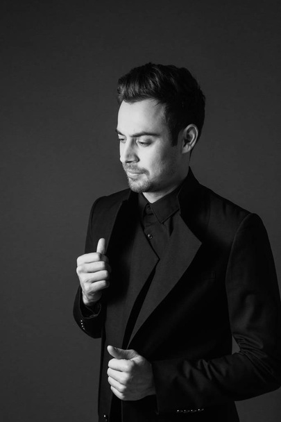 Ceket, düz studio arka plan üzerinde siyah ve beyaz elbiseli, ayakta ve tarafından bakarım genç yakışıklı bir adam portresi eller. - Fotoğraf, Görsel