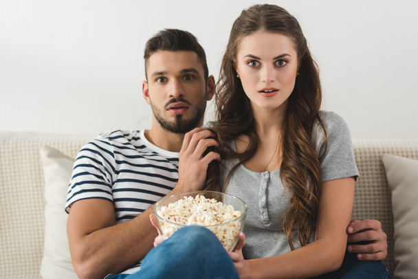 shocked couple with bowl of popcorn watching movie at home - Photo, Image