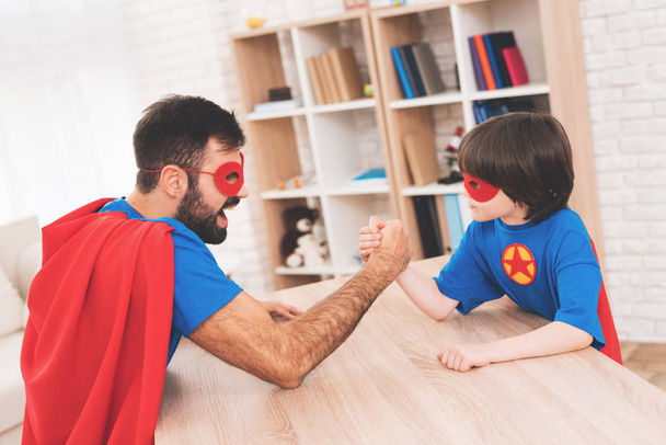 Father and son in suits of superheroes. They compete in armwrestling. They are measure their strength - Foto, Imagem