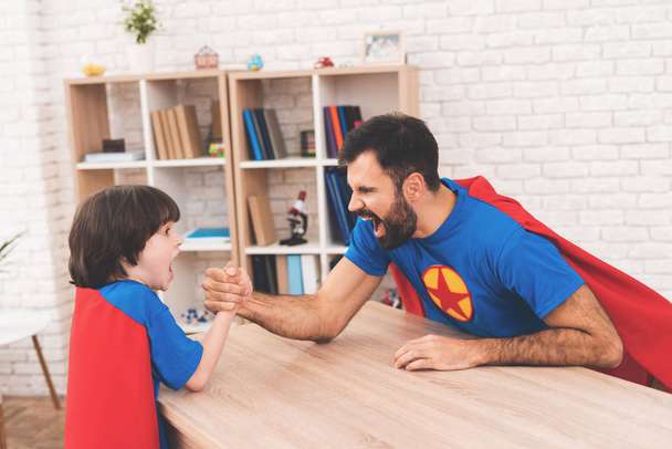 Father and son in suits of superheroes. They compete in armwrestling. They are measure their strength - Photo, Image