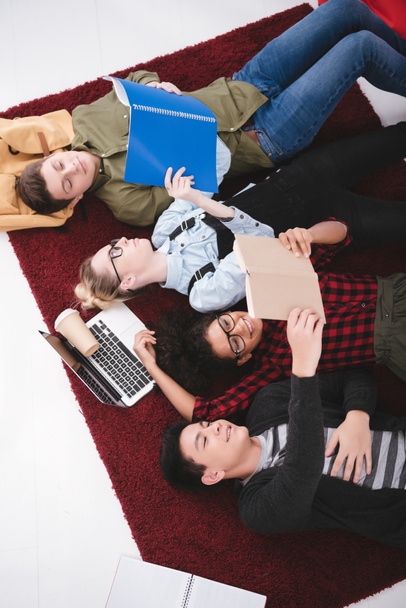 young teen students lying on carpet with notebooks and laptop - Photo, Image