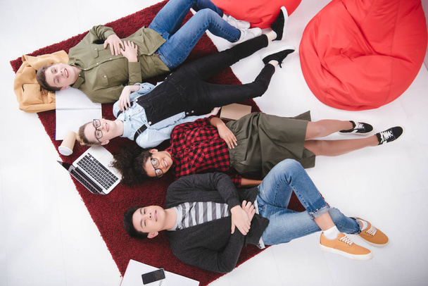 young teen students lying on carpet with notebooks and laptop - Foto, Imagem