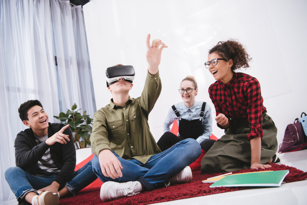 Junge mit Virtual-Reality-Brille sitzt mit Freunden auf Teppich - Foto, Bild