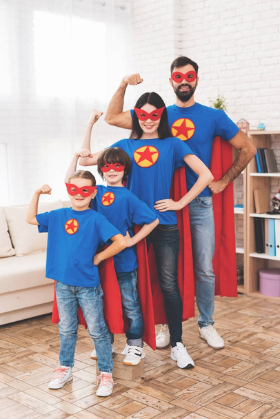 Молода сім'я в червоно-синіх костюмах супергероїв. Їхні обличчя в масках і вони в плащах
. - Фото, зображення