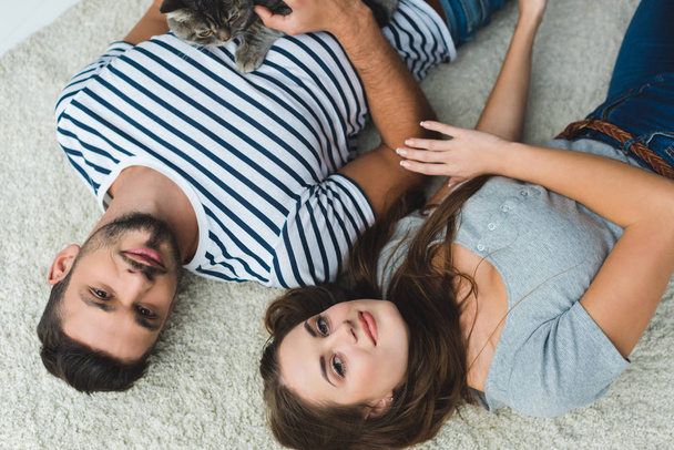 top view of young couple lying on floor with cute tabby cat - Φωτογραφία, εικόνα