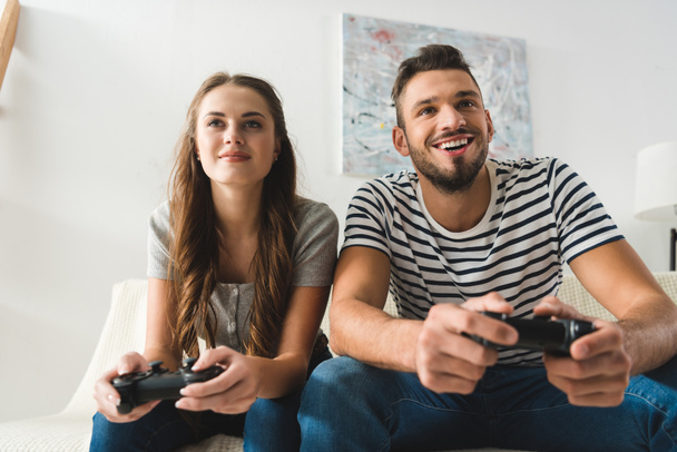 happy young couple playing games with gamepads at home - Fotó, kép