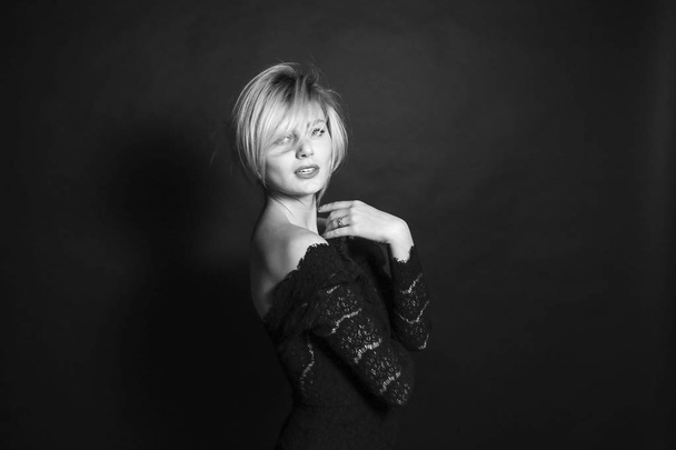 Schwarz-Weiß-Porträt einer jungen Frau in einem Spitzenkleid, die eine halbe Drehung zur Kamera vor einem schlichten Studiohintergrund steht - Foto, Bild