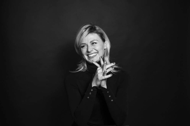 Schwarz-Weiß-Porträt einer jungen Frau, lachend, zur Seite blickend, Händchen haltend, vor schlichtem Studiohintergrund - Foto, Bild