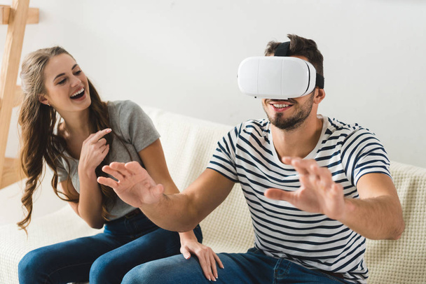 laughing young woman pointing at her boyfriend using vr headset - 写真・画像