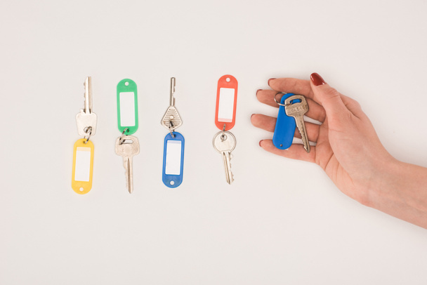 bovenaanzicht van de hand met kleurrijke etiketten geïsoleerd op de witte knop ingedrukt naast set sleutels voor het - Foto, afbeelding