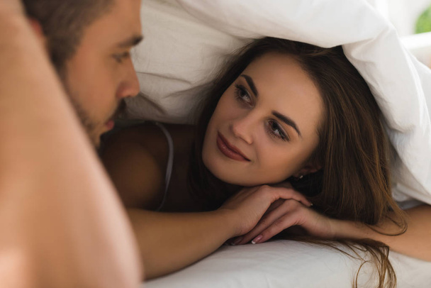 young couple under blanket looking at each other in bed - Foto, imagen