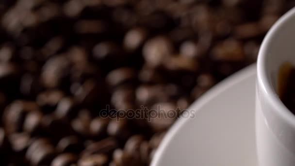Pouring coffee from coffee pot in white cup surrounded by coffee beans. - Séquence, vidéo