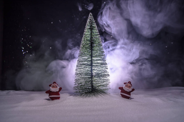 Happy Santa Claus panenku včas vánoční strom a sněhu. Bokeh barevné pozadí. Santa Clause a veselé Vánoce modelu obrázek toy na tmavém tónovaný - Fotografie, Obrázek