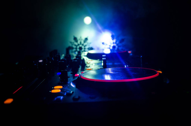 Dj mixer with headphones on dark nightclub background with Christmas tree New Year Eve. Close up view of New Year elements or symbols (Santa Clause, Snowman, Dog 2018, gift box) on a Dj table. toned - Photo, image