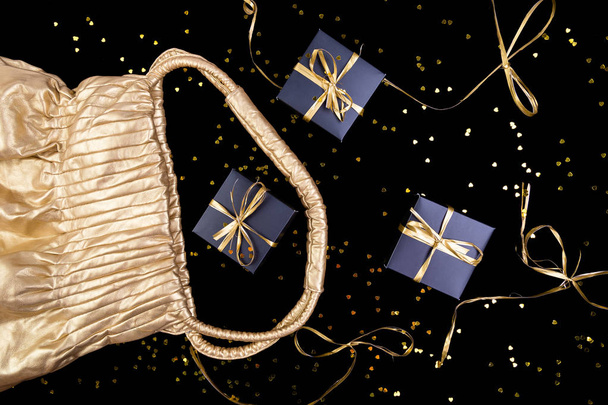 schwarze Geschenkboxen mit goldenem Band aus goldenem Beutel auf glänzendem Hintergrund. flache Lage. - Foto, Bild