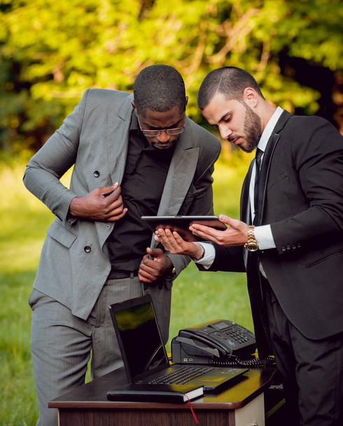 Two young multicultural businessmen at work in park. Concept of remote work. - Foto, afbeelding