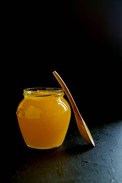 Honey bee in a jar with a wooden spoon. - Zdjęcie, obraz