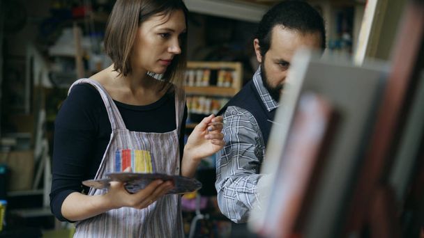 Skilled artist man teaching young girl to draw paintings and explaining the basics in art studio - Φωτογραφία, εικόνα