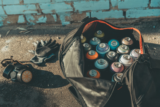 guantes y respirador cerca de la bolsa grande con latas de pintura en aerosol
 - Foto, Imagen