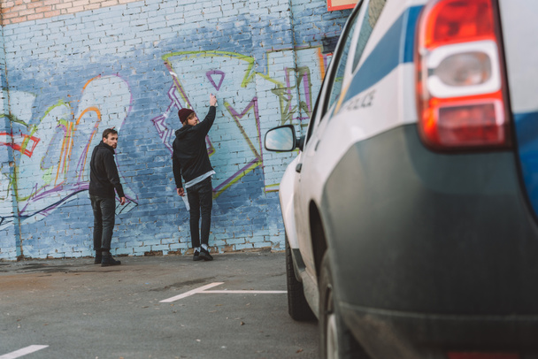 Powrót widzenia wandali malowania graffiti na ścianie, samochód policyjny na pierwszym planie - Zdjęcie, obraz