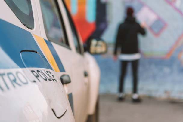 vista trasera de graffiti de pintura vándalo en la pared, coche de policía en primer plano
 - Foto, Imagen